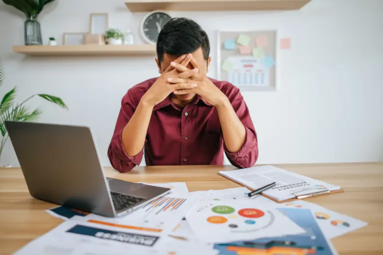 seorang pria yang memegang kepala karena pusing kerjaan di depan laptop